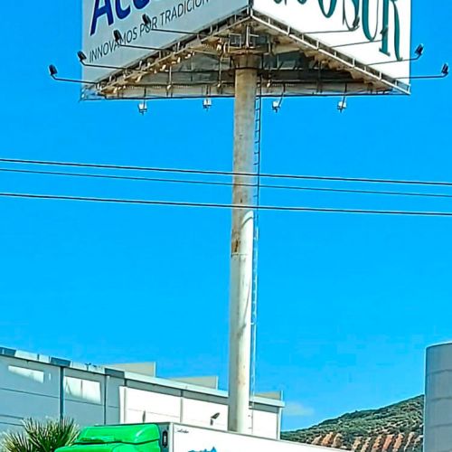 Camión verde con remolque blanco junto a letrero alto de Acesur Coosur